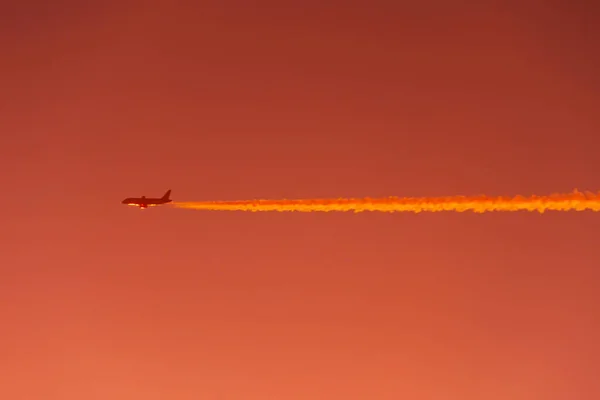 비행기는 때붉은 오렌지 하늘의 곳에서 대조적 자취를 남기며 하늘을 비행기 — 스톡 사진