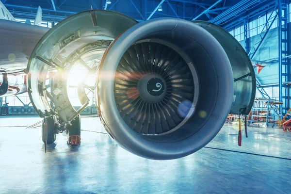 Kaputu açık olan jet motoru, hangar kapısının arkasındaki parlak ışıkla aydınlatılıyor.