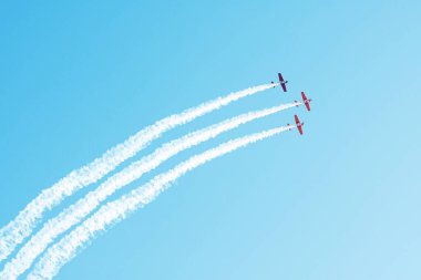 Mavi gökyüzünde duman bulutu içinde uçan üç hafif motor uçağı.