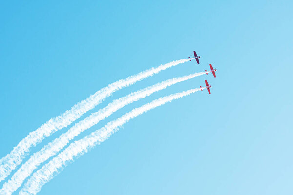 Три лёгких самолёта летят в облаке дыма в голубом небе.