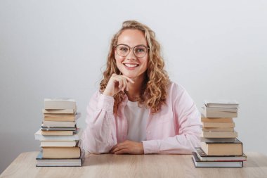 Güzel genç öğrenci iki kitap yığınının arasında oturuyor.
