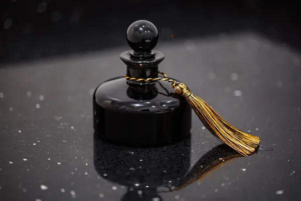 Eine schwarze Flasche mit rundem Korken und goldenem Pinsel auf schwarzem Hintergrund — Stockfoto