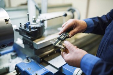 Torna tezgahına yakın bir işçinin ellerinde elektronik metal kalınlığı ölçer.