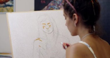 Ev stüdyosunda ağır çekimde portre üzerinde çalışan genç bir sanatçının el kamerasıyla çekilmiş görüntüsü. Çekici kız, üniversitede sanat eğitimi alan sanat eserleri çiziyor. Profesyonel araçlar bilgi ana sınıfı 