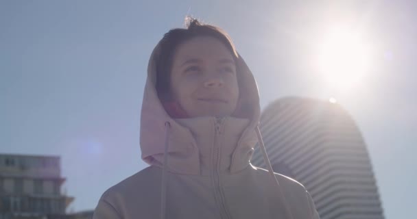 Mujer joven y bonita sonriendo en el fondo de los grandes edificios de la ciudad. Chica feliz disfrutando de la vida y respirando aire fresco de pie en medio del paisaje urbano de la ciudad. Concepto de éxito y motivación — Vídeo de stock