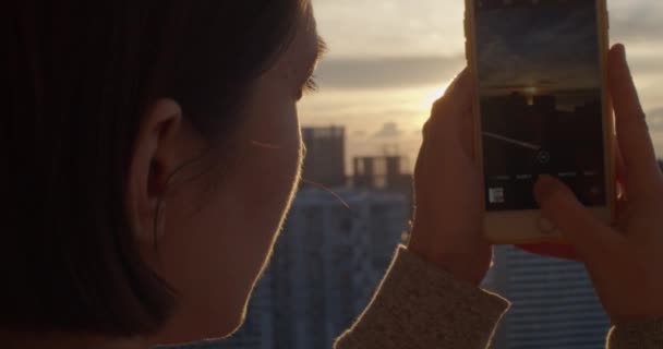 Giovane donna scattare foto di tramonto con dispositivo smartphone primo piano. Ragazza godendo bella vista del paesaggio urbano e fotografare edifici e architettura la sera. Fotografia cellulare — Video Stock