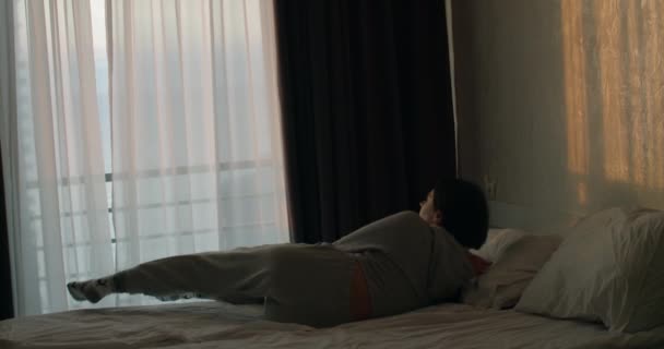 Young Caucasian woman waking up and opening curtains after taking a nap back rear view. Attractive relaxed girl greeting new day in early morning looking outside and enjoying view in hotel room — Stock Video