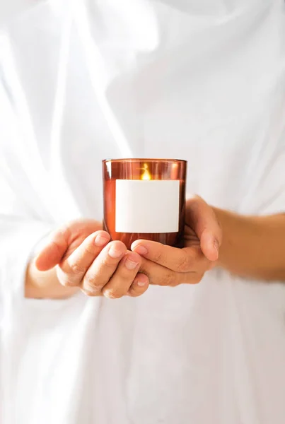 Woman in white clothing holding burning candle close-up. Church poster. Mock up for candle shop. Space for text or logo branding. Stories format advertising aromatherapy or candle handmade masterclass