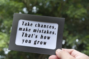 Motivational and inspirational quote on hands holding framed paper with blurred green tree background - Take changes, make mistakes, that is how you grow