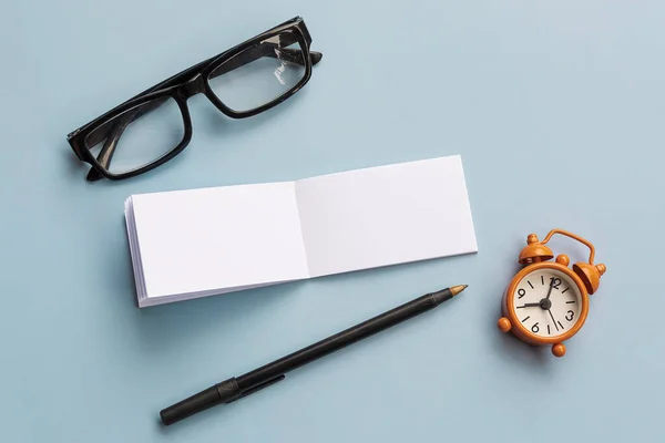 Bloc Notas Con Gafas Lectura Bolígrafo Despertador Sobre Fondo Azul — Foto de Stock