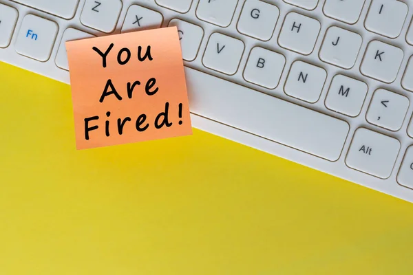 You\'re Fired text on orange sticky note on top of white keyboard. Human Resource and contract concept.