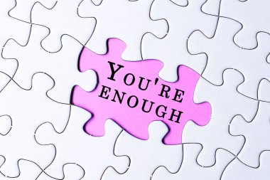 White jigsaw puzzle with motivational and inspirational quote over purple background - You're enough.