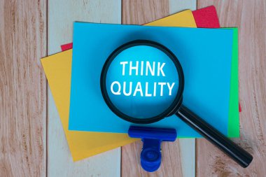 Ahşap masanın üzerinde büyüteç olan Renkli Yapışkan Not Kalitesini Düşün. İş Konsepti.