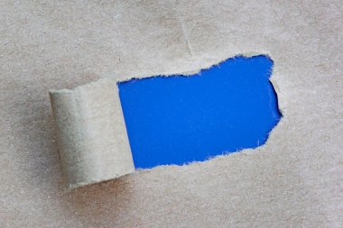 Mavi arkaplandaki kahverengi kağıttaki yırtık delikte metin. Uzayı kopyala Düz yatıyordu. Tam üstte.