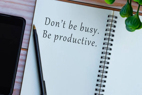 Motivational and inspirational quote on note book on wooden desk - Don't be busy, be productive.