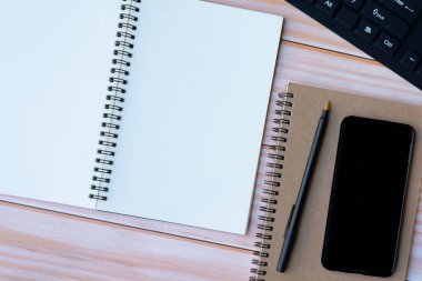 Tahta masadaki not defteri, kalem, akıllı telefon ve klavyenin tam üstünde. Düz yatıyordu. Boşluğu kopyala.