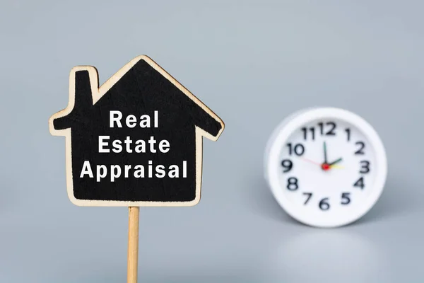 Real Estate Appraisal text on wooden house model with blurred white alarm clock background. Real estate investment concept.