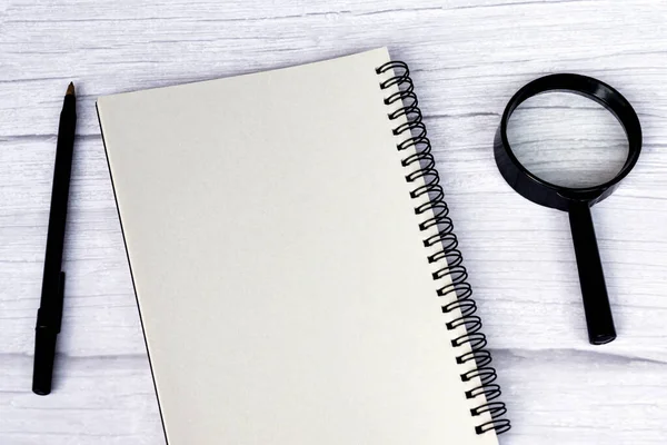 Blank notepad with pen, and magnifying glass on a white wooden table. Flat lay. Directly above. Copy space.