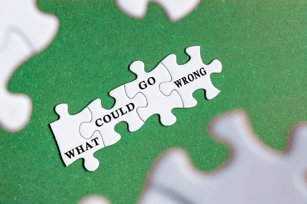 What could go wrong text on white jigsaw puzzle with some missing pieces on wooden background.