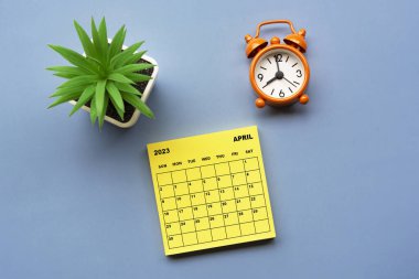 Nisan 2023 'te, üzerinde saksı bitkisi ve alarm saati bulunan Yapışkan Not takvimi saat 8' de mavi arka planda. İş konsepti.
