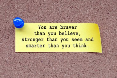 Motivational quote on stick note and pinned to a cork notice board - You are braver than you believe, stronger than you seem and smarter than you think.