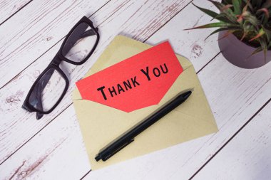 Thank you text on red card with envelope on wooden desk.