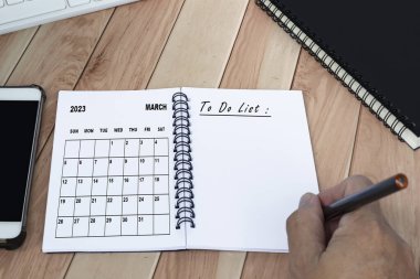 Businessman hands with pen writing to do list with March 2023 calendar on notebook. Copy space. Business concept.
