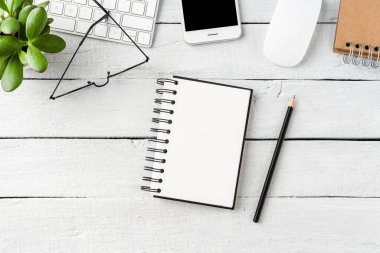 Ofis masaüstü boş defterle beyaz ahşap masa ve iş aksesuarları. Üst görünüm