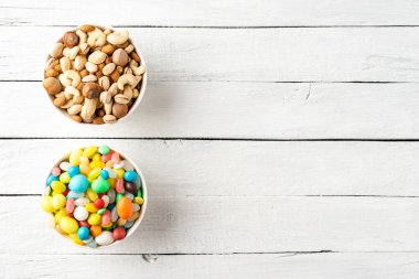 Sağlıklı ve sağlıksız atıştırmalıkların karşılaştırılması. Fındık ve tatlı karışımı beyaz ahşap arka plandaki kaseler ve kopyalanmış alan
