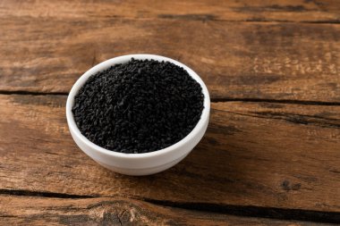 Eski ahşap arka planda kasede siyah kimyon tohumları