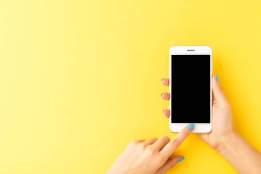 Sarı arka planda boş ekranı olan cep telefonu kullanan kadın elleri. Üst görünüm