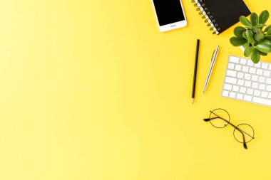 Sarı arka planda iş aksesuarları ve kopyalama alanı olan şık bir ofis masası. Üst görünüm