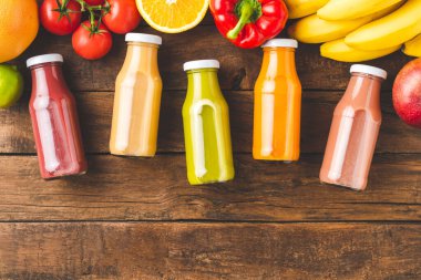 Meyve ve sebzeli ahşap masada şişelerde taze meyve suyu içerek.