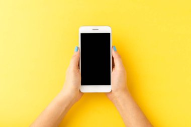 Sarı arka planda boş ekranlı, cep telefonlu bir kadının el resmi. Üst görünüm