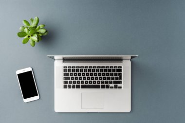 Gri masada dizüstü bilgisayarı ve cep telefonu olan bir ofis masası. İş geçmişi. Düz yatıyordu