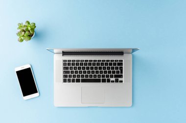 Laptop ve akıllı telefon mavi arkaplanda ve kopyalanmış. Ofis masaüstü. Üst görünüm