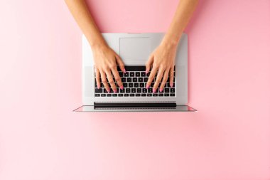 Pembe arka planda dizüstü bilgisayar kullanan kadın eller. Ofis masaüstü. Üst görünüm