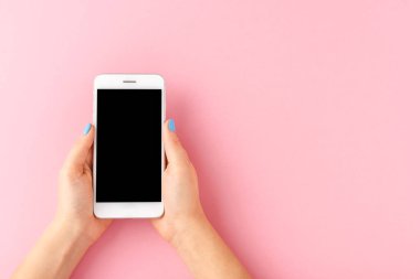 Pembe arka planda boş ekranı olan akıllı telefonu tutan kadın eller. Üst görünüm