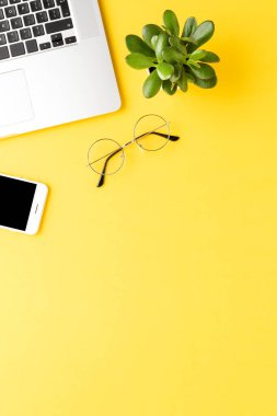 Sarı arka planda dizüstü bilgisayarı ve aksesuarları olan bir ofis masası. Üst görünüm