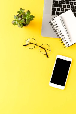 Bilgisayarı, cep telefonu ve sarı arka planda iş aksesuarları olan bir ofis masası. İş konsepti