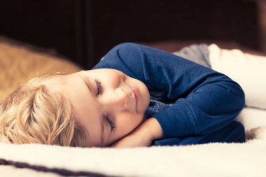 Cute kid taking a nap while resting on the bed with eyes closed. 
