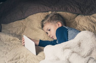 Small kid using digital tablet and watching something on the internet before bedtime. 