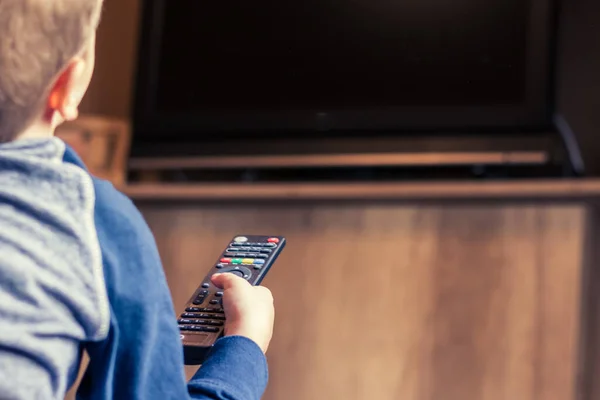 Close-up of child watching TV and changing channels with remote control at home.