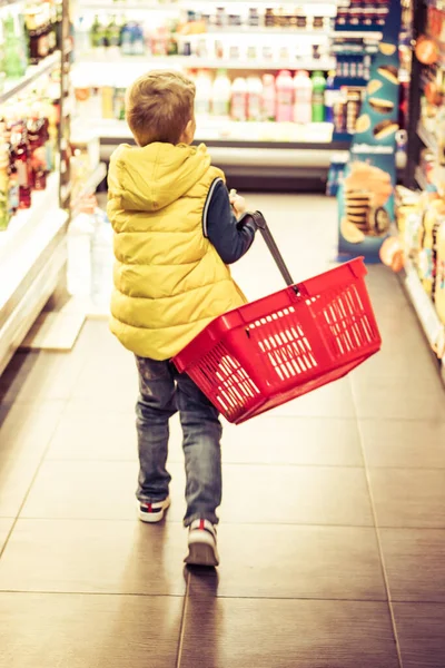 Rear view of boy with shopping basket walking through supermarket. 