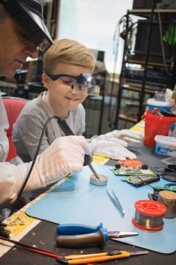 Teacher and his student using soldering iron and repairing circuit board in tech laboratory.