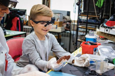 Little boy analizyng computer part with help of IT teacher during school science project in tech laboratory.