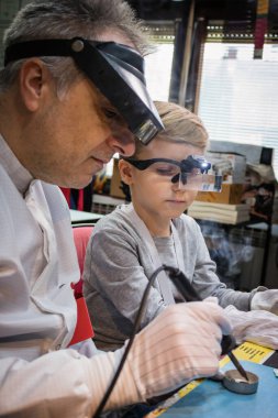 Science teacher is showing to his student how to solder in a tech laboratory during scientific experiment.