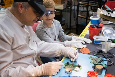 Science teacher is teaching his student to repair circuit board in IT laboratory.