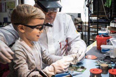 Happy kid learning how to repair computer part with help of his teacher in tech laboratory. 