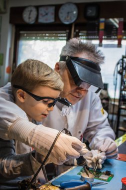 Little boy soldering and repairing circuit board with help of a teacher in IT laboratory. 